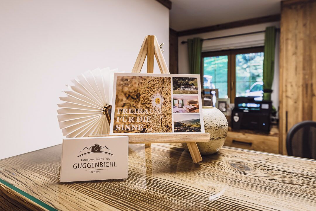 A wooden table with a framed book, a fan, and a sign for GUGGENBICHL.