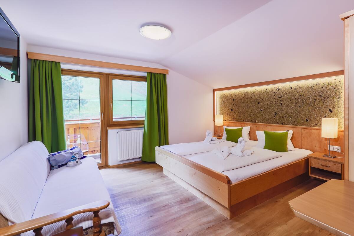 Quarto com cama, sofá, mesa de cabeceira de madeira e luminária fixada na parede.