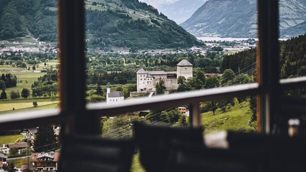 Un espace repas offrant une vue sur un paysage montagneux, avec notamment une structure ressemblant à un château.