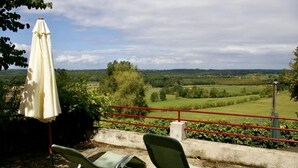 Une terrasse avec deux chaises vertes et un parasol blanc, d’où l’on peut admirer un paysage rural.