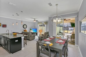 Een moderne keuken met een centraal eiland, een eetgedeelte met een grote tafel en een woonkamer met een bank en televisie.