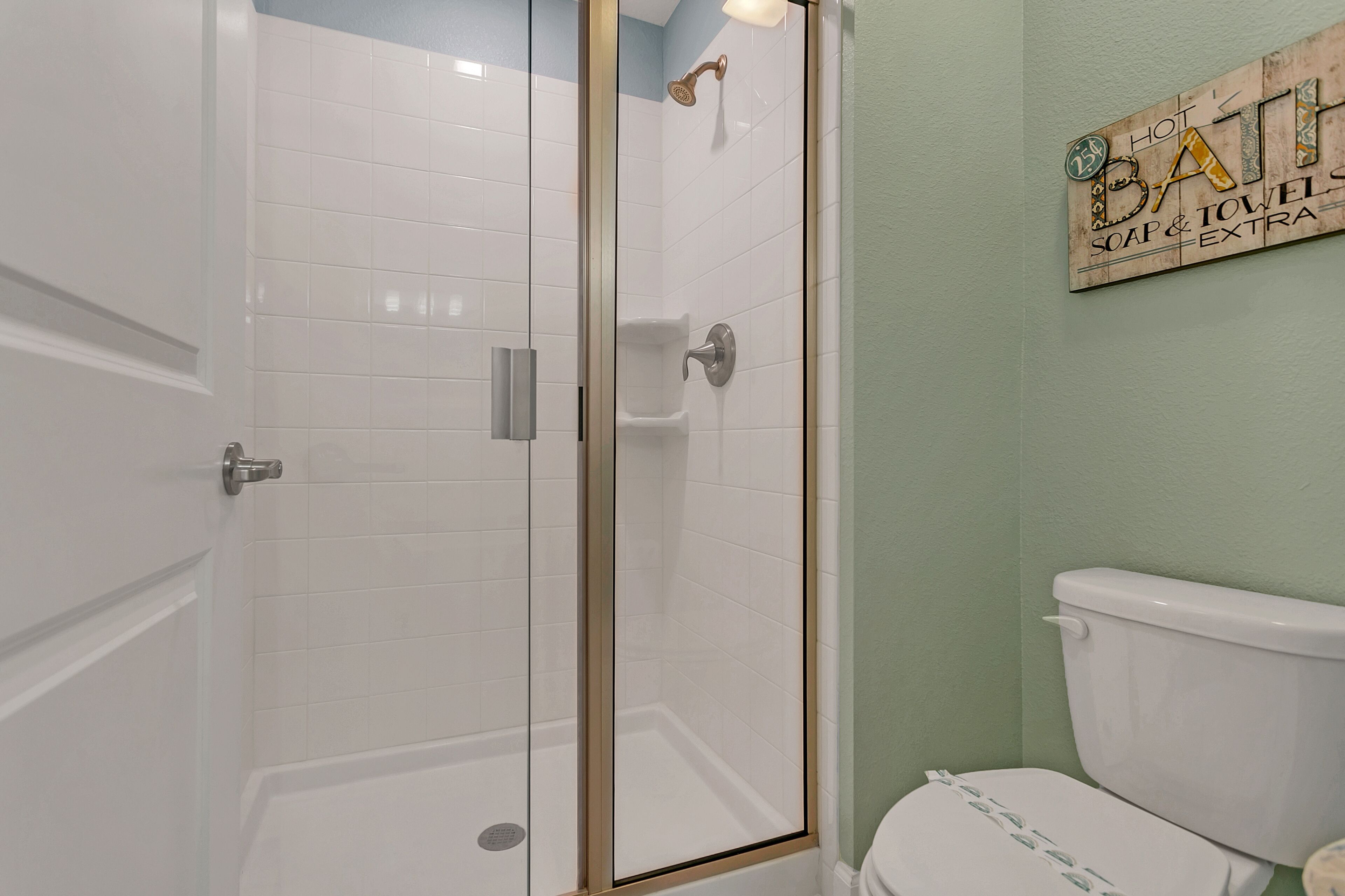 A bathroom with a glass-enclosed shower, a white toilet, and a sign advertising 'HOT BATHS, SOAP & EXTRA TOWELS'.
