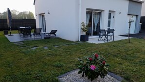 A modern house with a patio area featuring outdoor seating and a garden with a flower bed. - 3* HOUSE WITH GARDEN AND TERRACE (sleeps 8) in Pont-L'Abbe (Pont-l'Abbé)