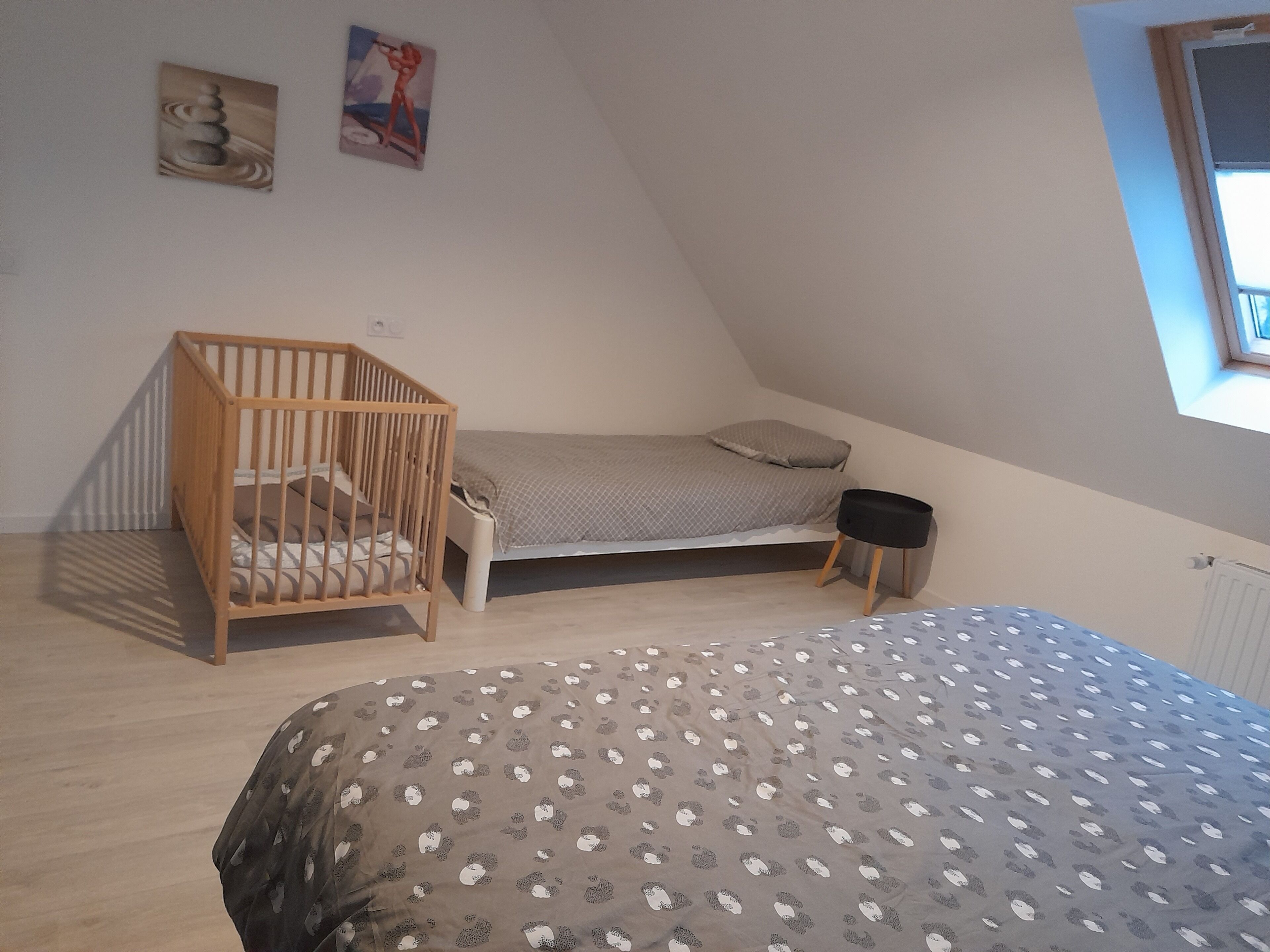 A bedroom with a sloped ceiling, a wooden crib, a single bed, and a small bedside table.