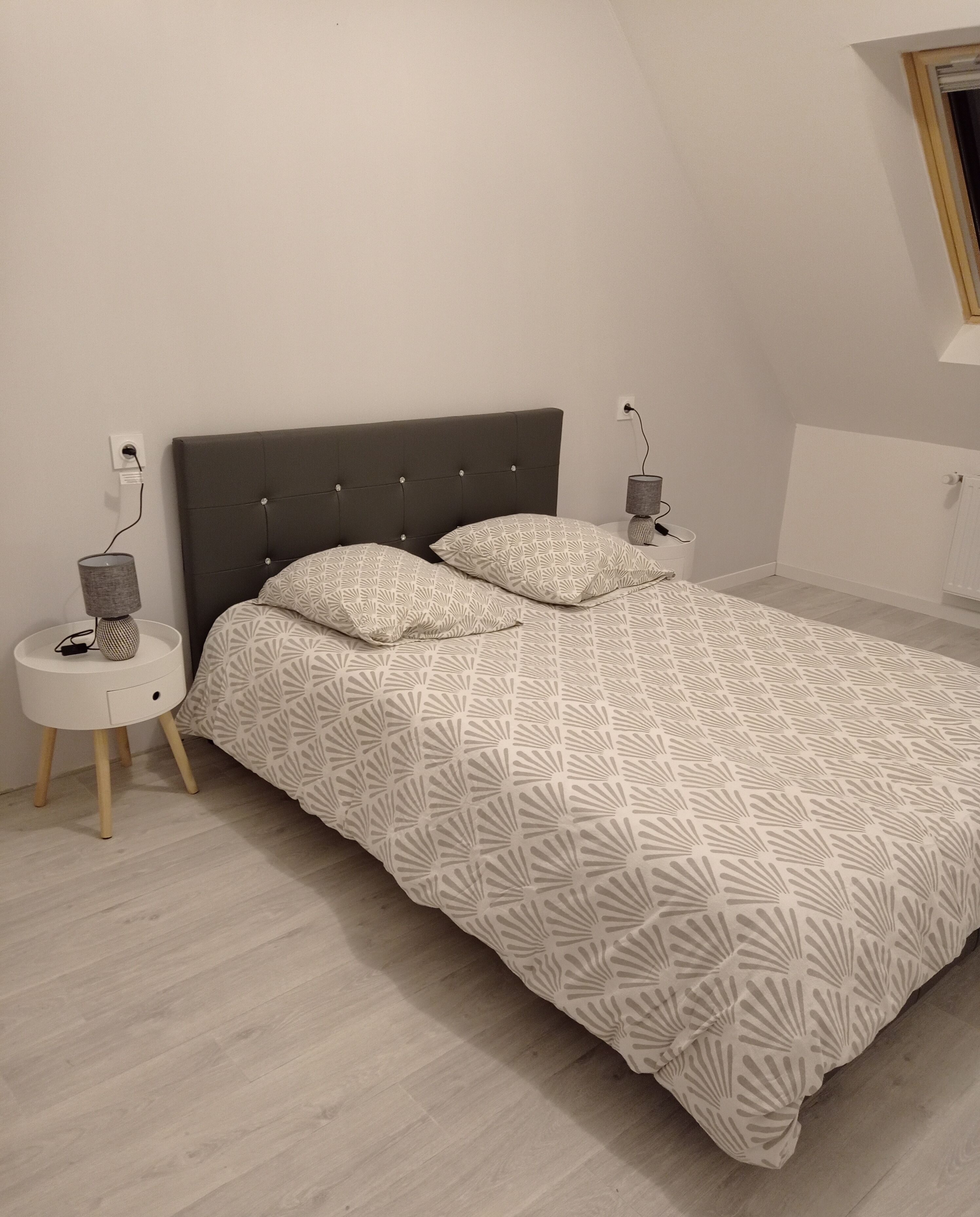 A bedroom with a bed, a bedside table, a lamp, and a radiator.