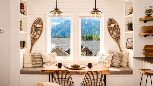 A cozy seating area with a table, chairs, and a view of mountains through large windows.