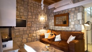 Ein gemütliches Wohnzimmer mit einer Steinwand, einem braunen Ledersofa, einem Holztisch, einer Gitarre und einem Chandelier.