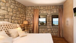 Ein Schlafzimmer mit einer Steinwand, einem Bett mit einer gebügelten Kopfteil, einem Nachttisch mit Lampe und Meerblick durch ein Fenster.