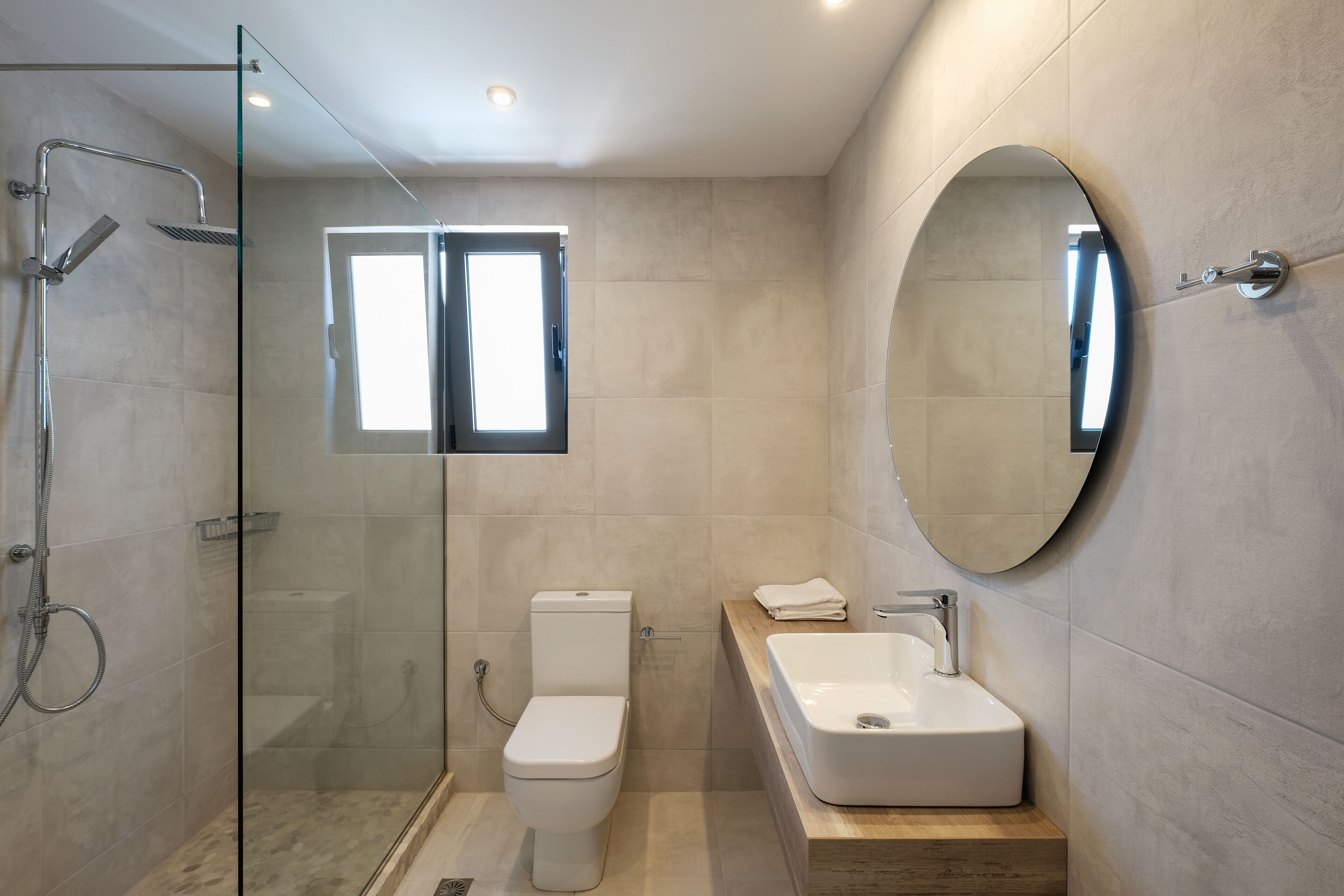 A modern bathroom with a glass-enclosed shower, a toilet, a sink with a mirror, and a window above the toilet.