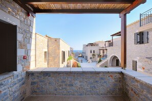 Un patio de piedra con vista al mar, edificios de piedra y una pérgola de madera.