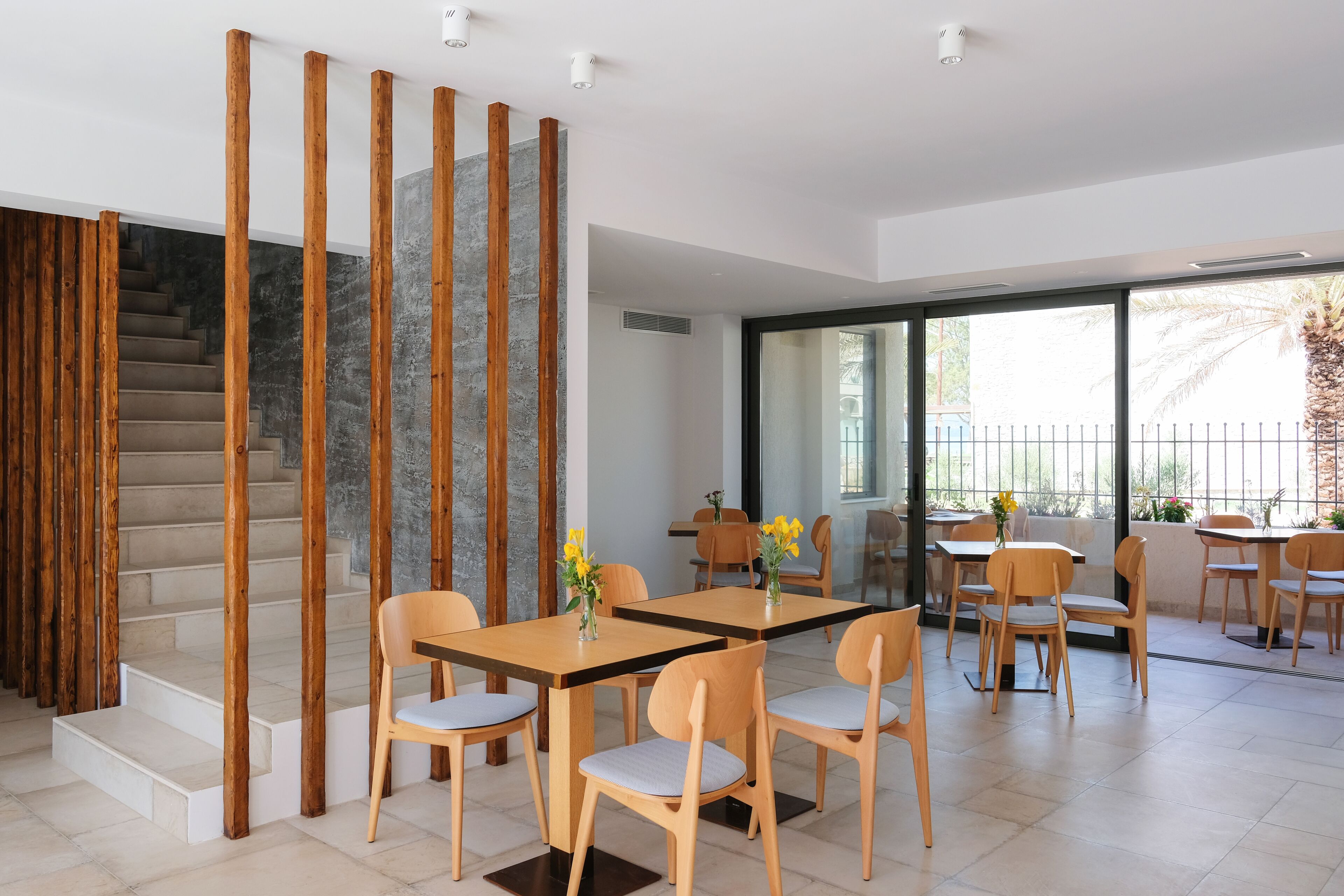 A modern interior with a staircase, wooden partitions, and a dining area with tables and chairs.