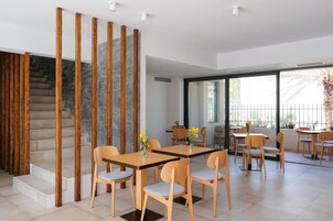 Un interior moderno con una escalera, separaciones de madera y una zona de comedor con mesas y sillas.