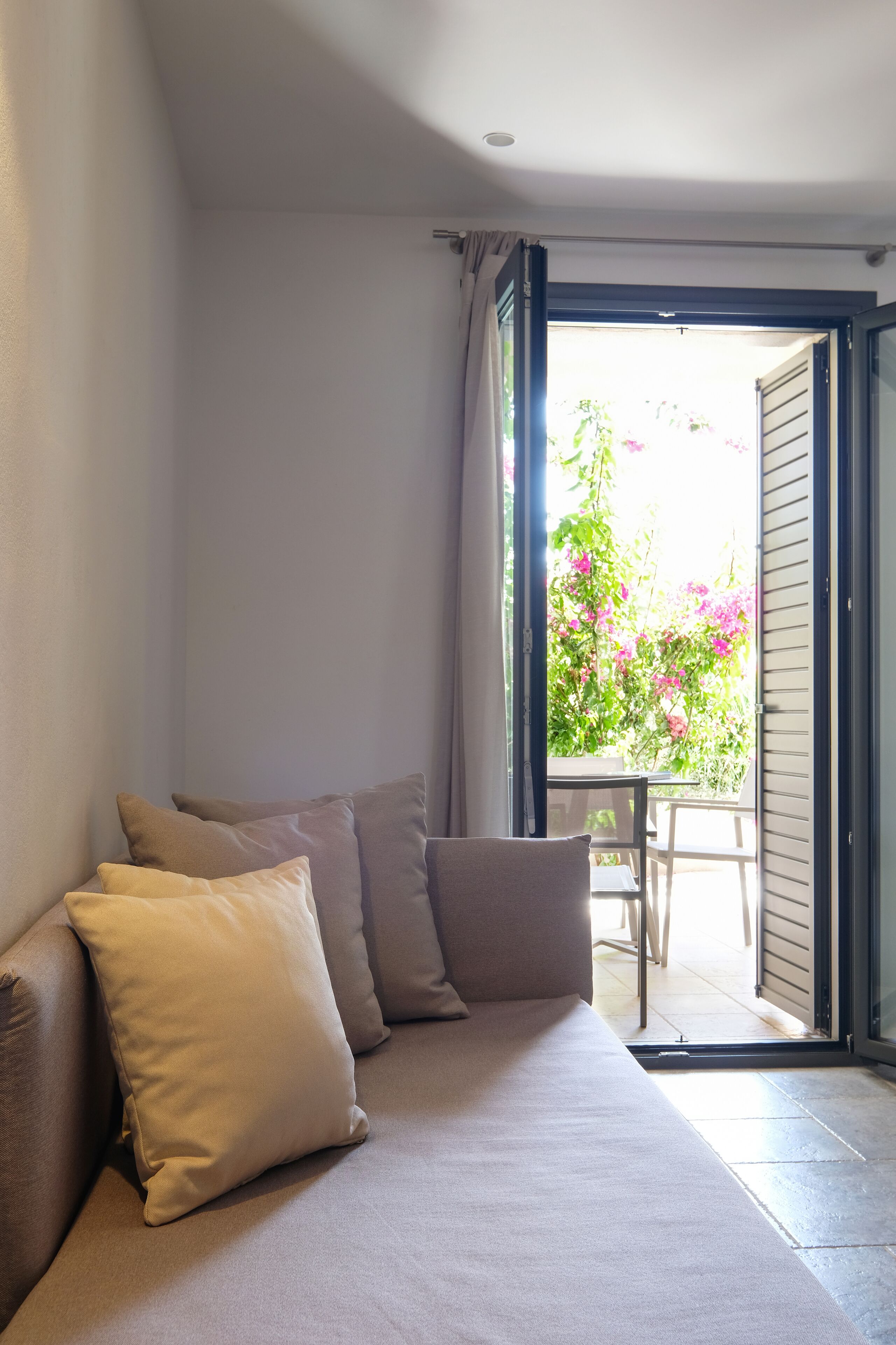 Una habitación con sofá, puerta corredera de vidrio que da a un espacio exterior con plantas y una mesa.