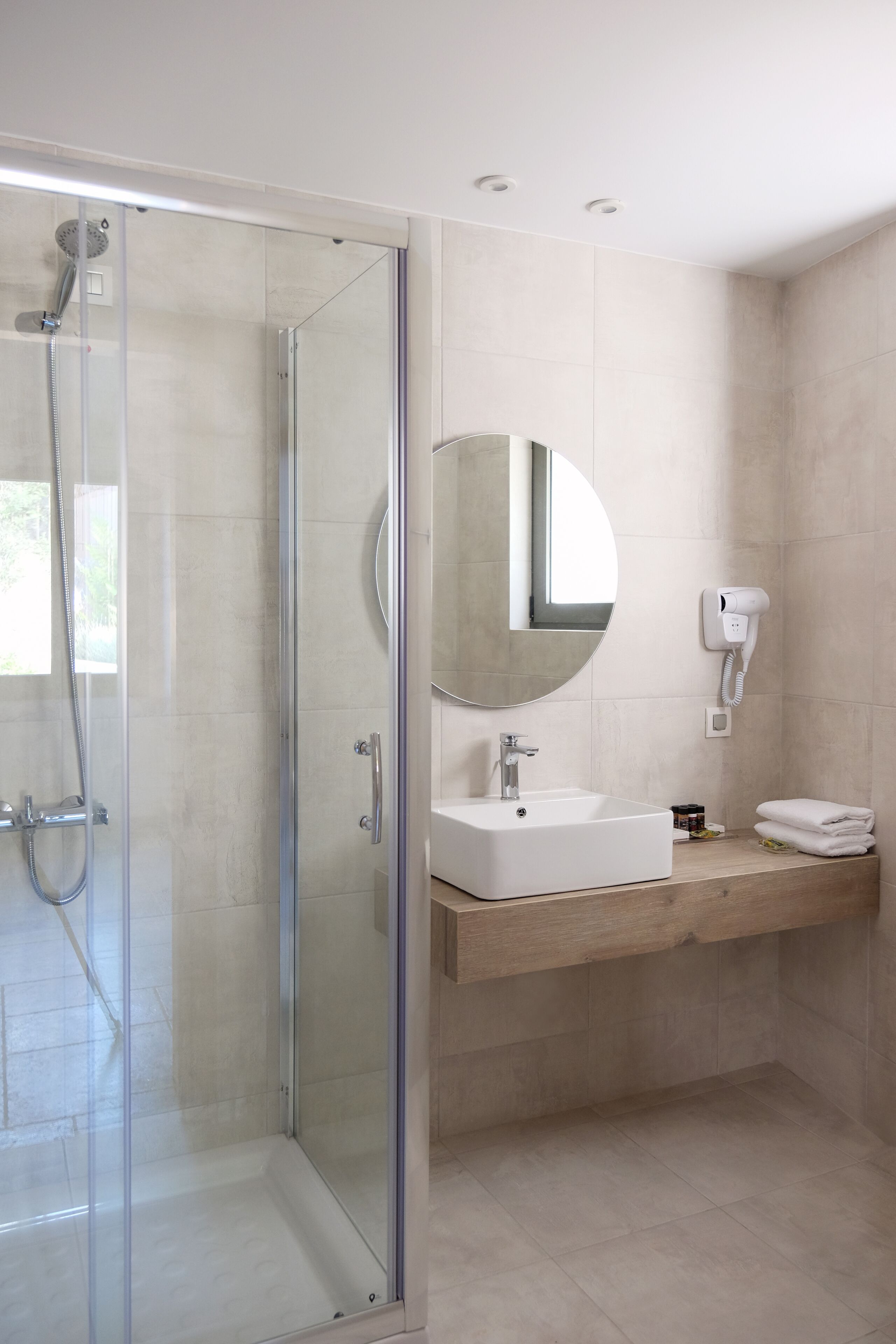 A modern bathroom with a glass-enclosed shower, a sink with a mirror, and a hairdryer mounted on the wall.