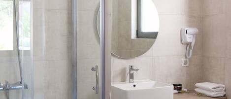 A modern bathroom with a glass-enclosed shower, a sink with a mirror, and a hairdryer mounted on the wall.