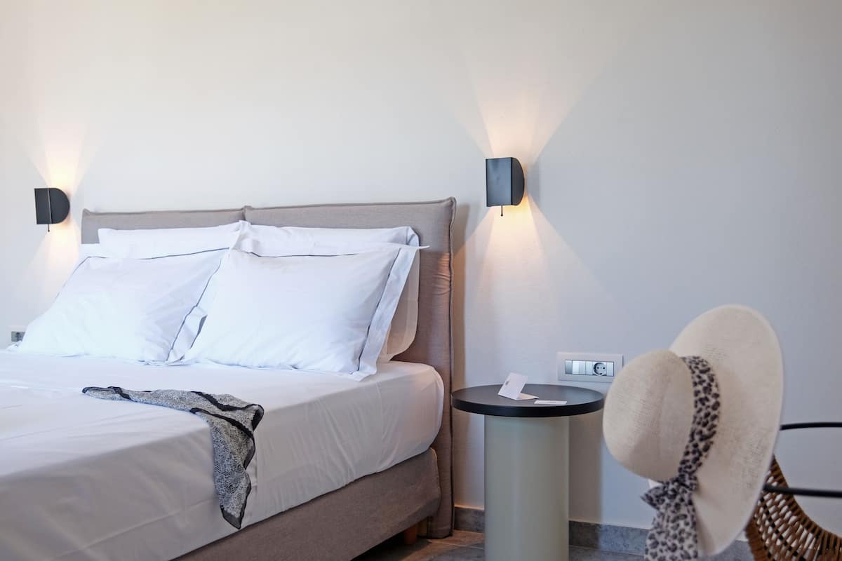 A neatly made bed with white linens, a grey headboard, and two wall-mounted light fixtures.