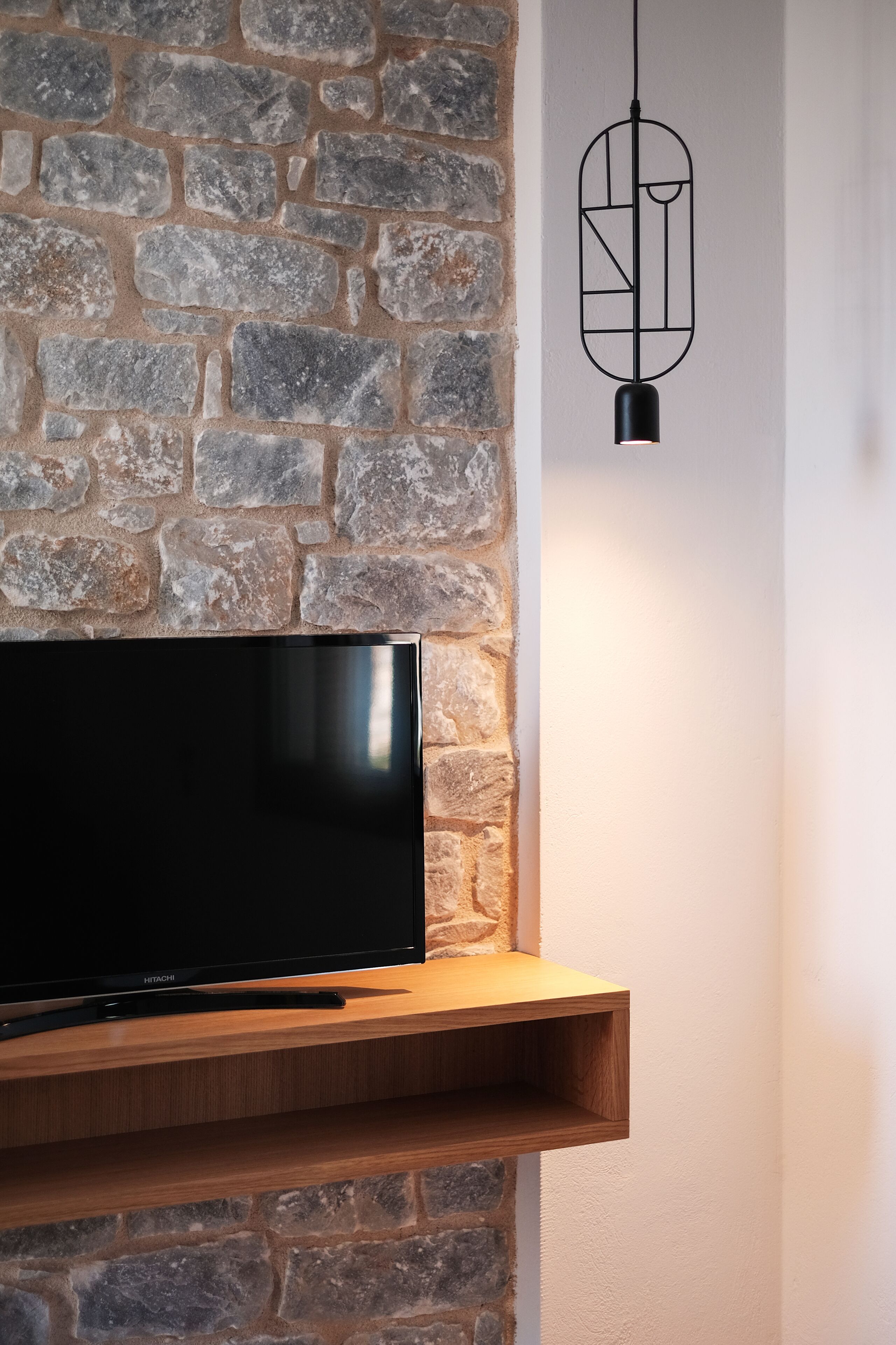 Ein Flachbildfernseher an einer Steinwand, darunter ein Holzregal.