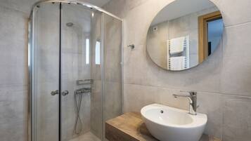 A modern bathroom with a glass shower enclosure, a round mirror, and a white sink with a wooden countertop.