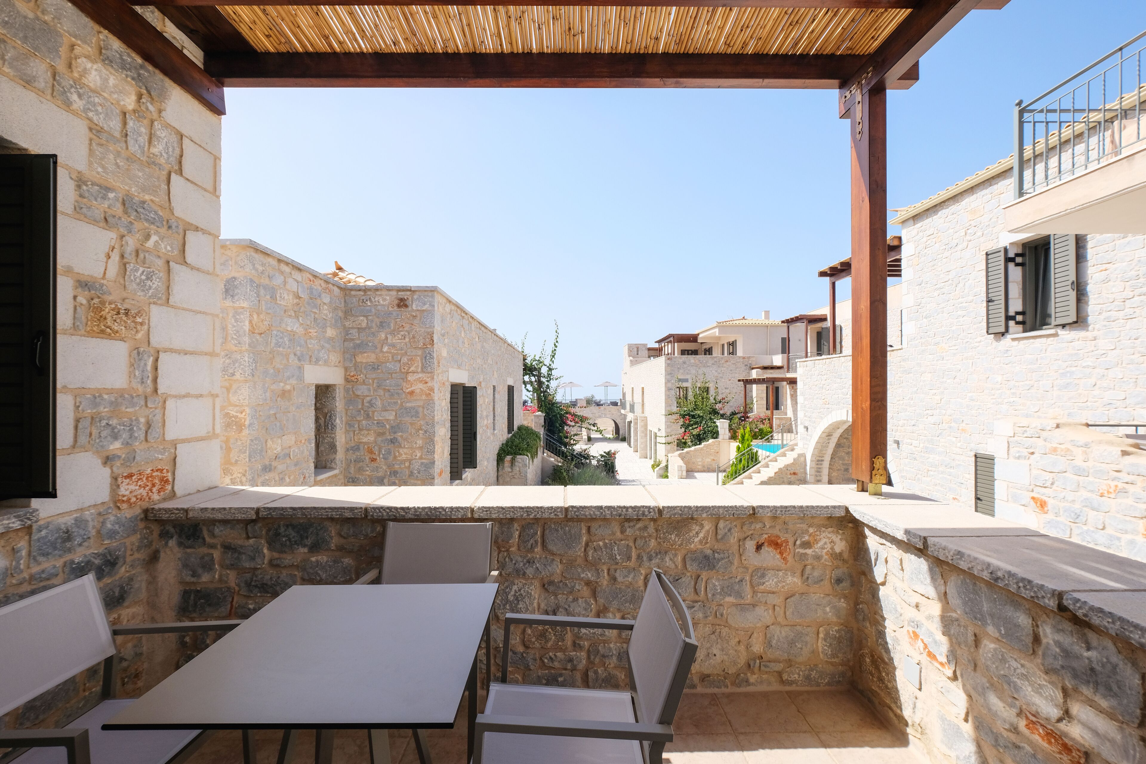 Un patio de piedra con mobiliario exterior, una pérgola de madera y vistas a edificios vecinos.