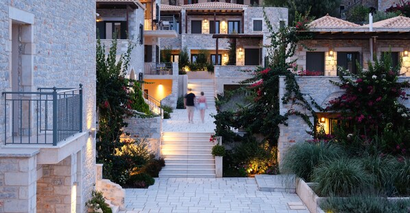 A courtyard with stone buildings, a central staircase, and lush greenery.