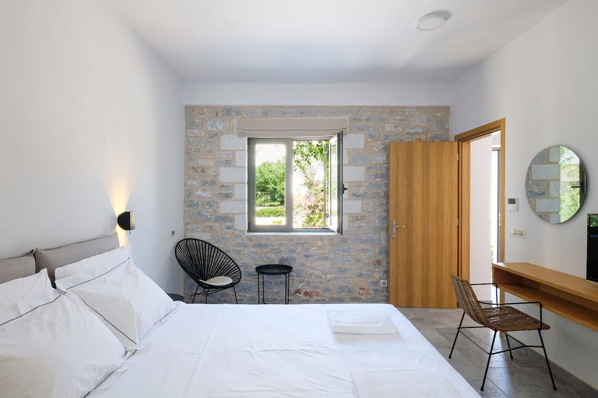 A bedroom with a bed, a chair, a desk, a window, and a door.