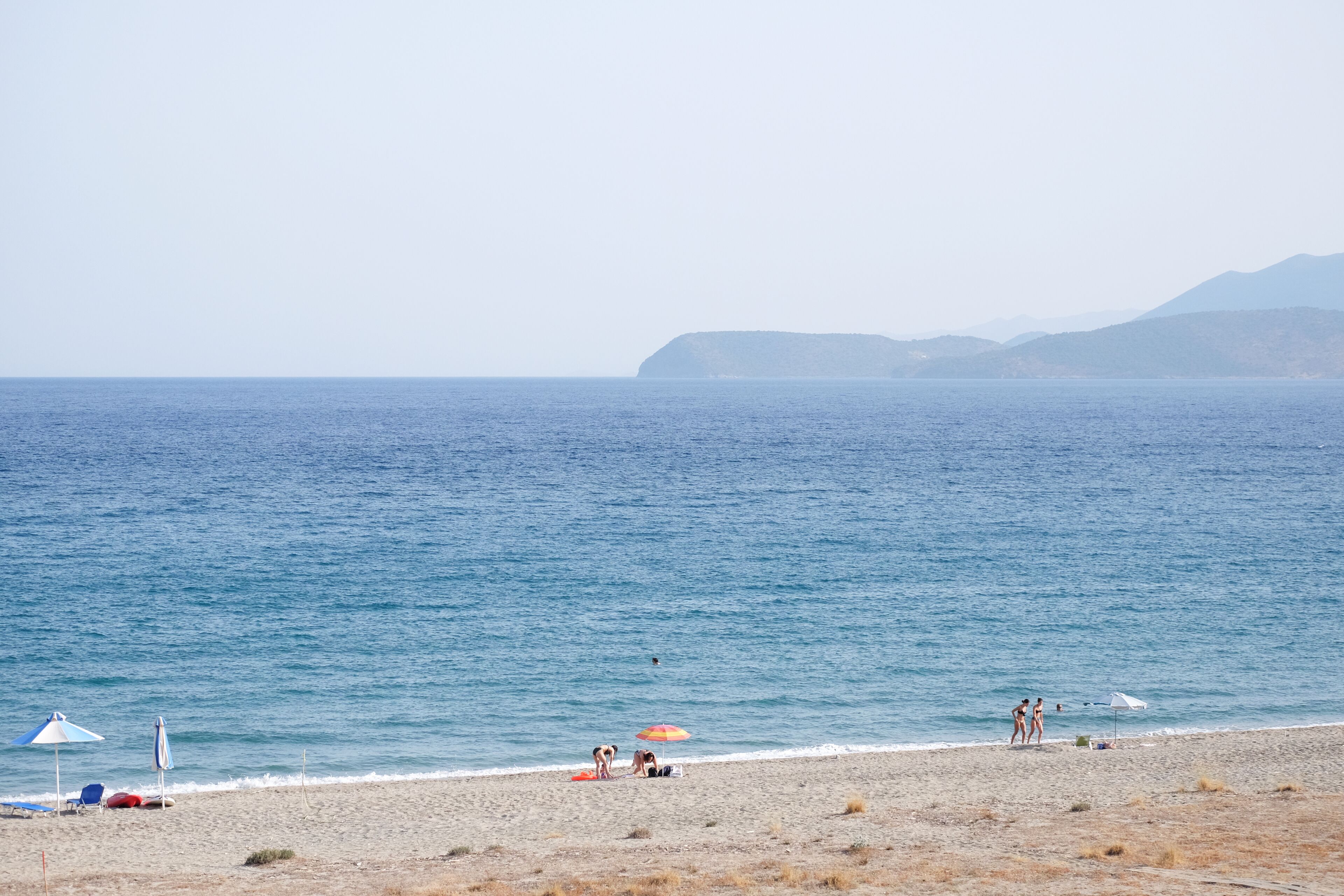 A beach with umbrellas and beach chairs, a clear sky, and a calm sea.
