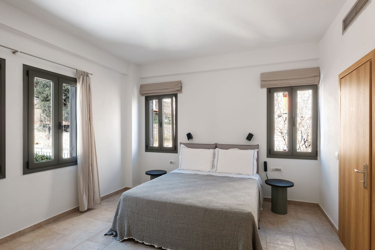 A bedroom with a bed, two bedside tables, a window with a curtain, and a door.