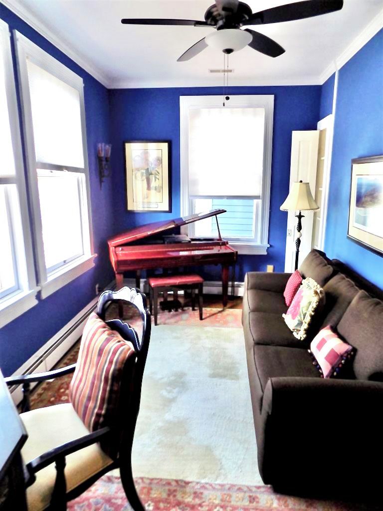 A living room with a piano, a sofa, a chair, and a ceiling fan.