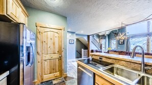A modern kitchen with a stainless steel refrigerator, wooden cabinets, a large island with a sink, and a chandelier. - Spacious Townhome with Private Hot Tub, minutes away from Winter Park Resort (Winter Park)