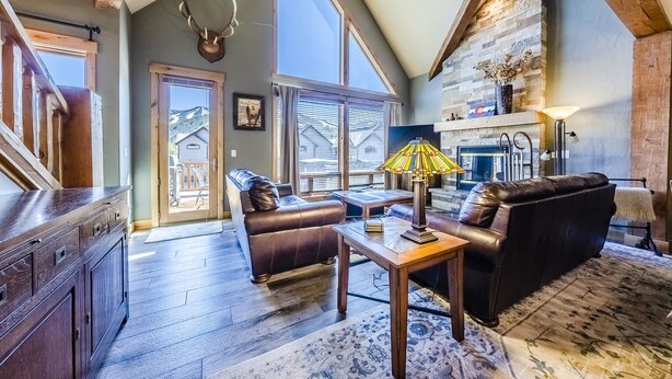 A spacious living room with a fireplace, leather sofas, and a large window overlooking a mountain. - Spacious Townhome with Private Hot Tub, minutes away from Winter Park Resort (Winter Park)