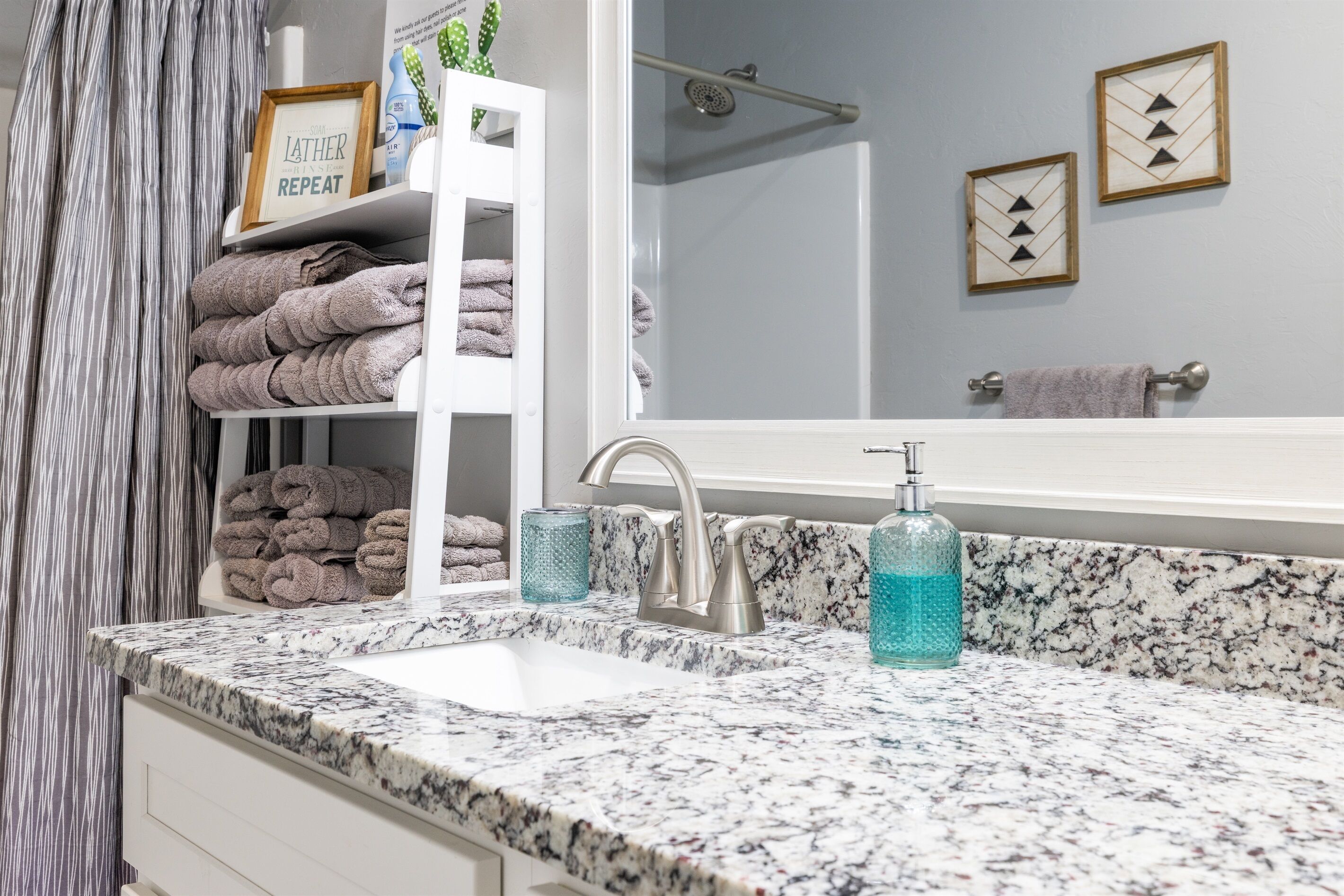 Un baño con encimera de mármol, un lavabo, un grifo, un dispensador de jabón de vidrio y un perchero con toallas dobladas.