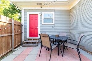 Une terrasse avec une table et des chaises, une porte rouge et une clôture en bois.