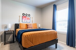 Une chambre à coucher avec un lit, une table de chevet, une fenêtre avec des rideaux et des éléments de décoration murale.
