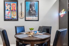 Un coin repas avec une table ronde, des chaises, une guitare, des affiches des Beatles encadrées et un panneau lumineux au néon.