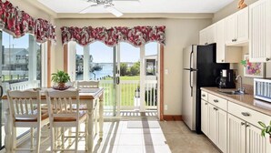 A kitchen with a view of a body of water, a dining area with chairs and a table, and a refrigerator.