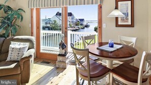 A room with a wooden floor, a brown sofa, a dining table with chairs, a potted plant, a view of a marina through a glass door, and a framed picture on the wall.