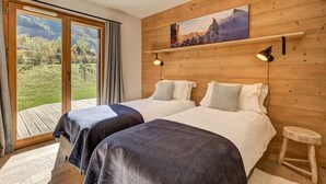 Slaapkamer met twee bedden, houten wanden, een groot raam met uitzicht op groen en een schilderij boven de bedden.