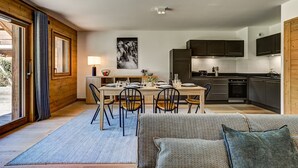 Een moderne keuken met donkere kasten, een eethoek met een houten tafel en stoelen, en een groot raam met gordijnen.