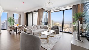 A modern living room with a sofa, coffee table, and dining area. Large windows offer a city view. - FIRST CLASS | 3BR | Burj Khalifa & Fountain view (Downtown)