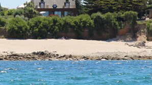 Une maison située sur la côte, dotée d’un balcon imposant, entourée d’une végétation luxuriante et bordée d’une côte rocheuse.