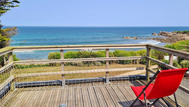 Une terrasse en bois avec une chaise rouge donnant sur une vue panoramique de la côte.
