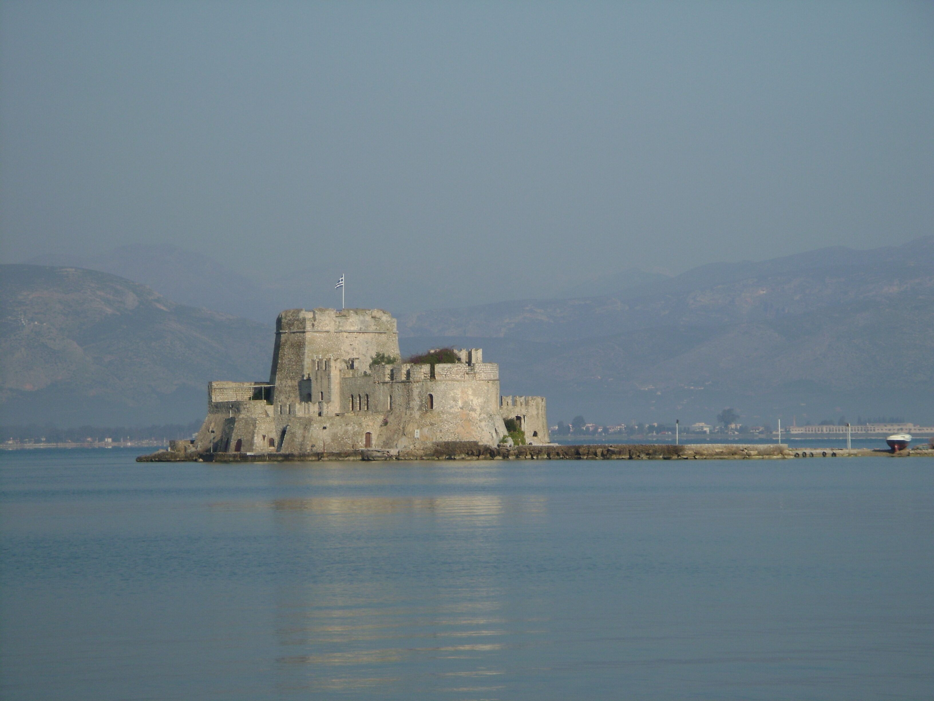 A historic stone castle with a flag on top, situated on an island in a body of water, surrounded by mountains.