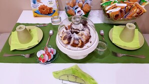 Een gedekte tafel met een kom dessert, borden, bestek en hapjes.