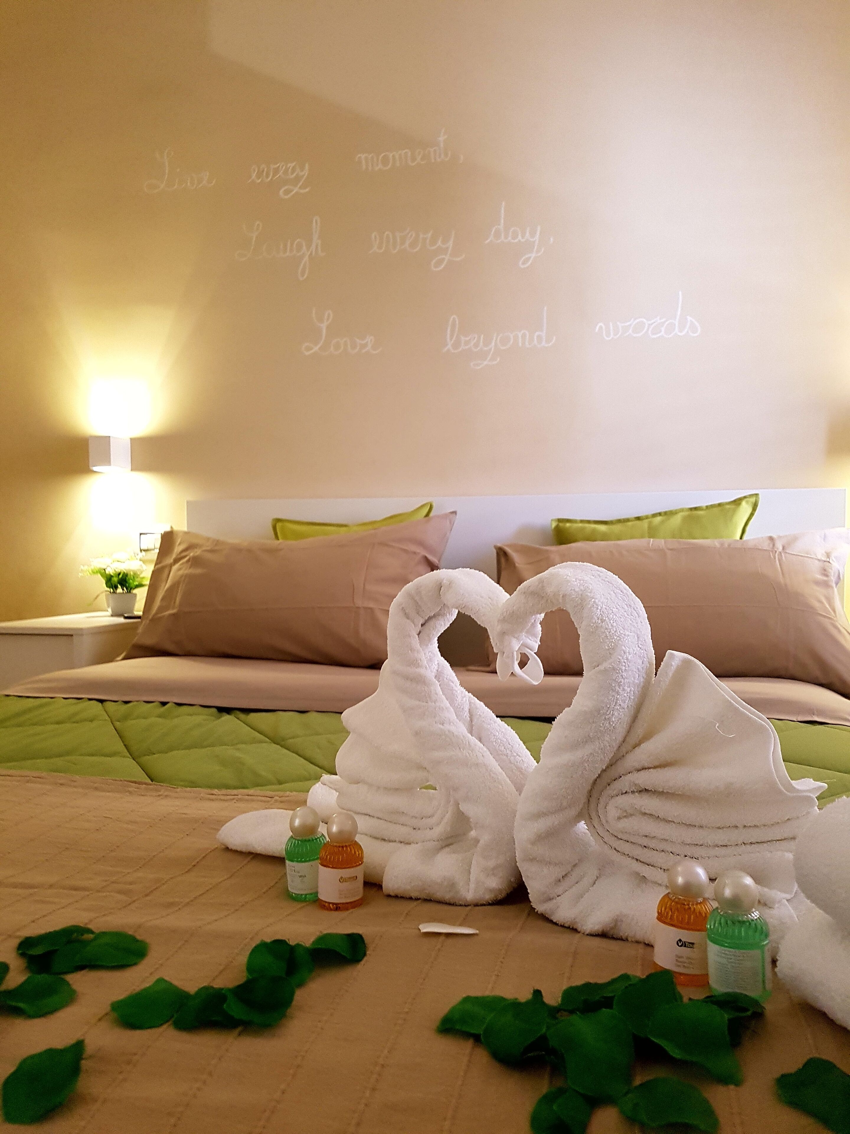 A hotel room with a bed, two swan-shaped towels, and a wall with inspirational quotes.