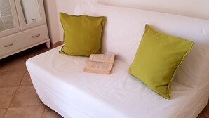 Een witte bank met twee groene kussens en een boek erop.