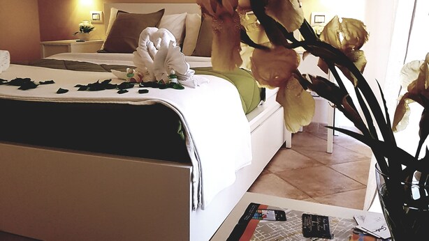 Hotelkamer met een bed, nachtkastje met een lamp, vaas met bloemen en een muur met een motiverende quote.