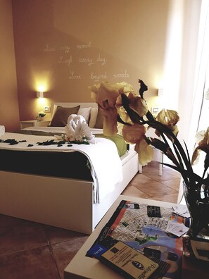 Une chambre d’hôtel avec un lit, une table de chevet avec une lampe, un vase de fleurs et un mur orné d’un texte inspirant.