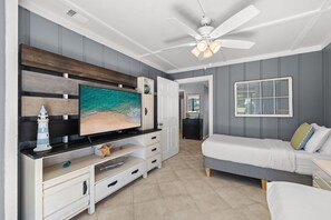 Quarto com televisão, cama, ventoinha no teto e vista para o exterior.