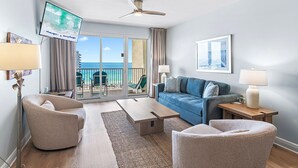 Ein modernes Wohnzimmer mit einer Couch, Sesseln, einem Couchtisch, einem Fernseher und einem Balkon mit Meerblick.