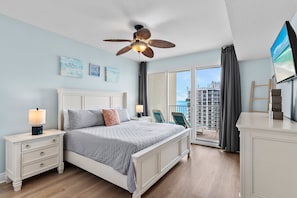 Un dormitorio con cama, mesita de noche, ventilador de techo y vistas a la ciudad.